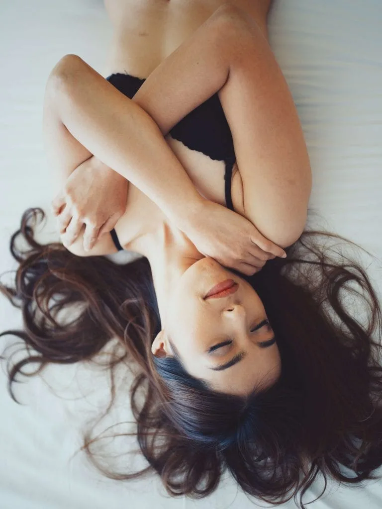 An image of one of our cam girls laid upside down on a bed in black lingerie.